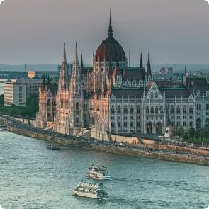 Vengrijos parlamento pastato su puošnia gotikos atgimimo architektūra Dunojaus upės pakrantėje Budapešte vaizdas iš oro. Upėje matomos valtys, o miesto vaizdas tęsiasi į foną.